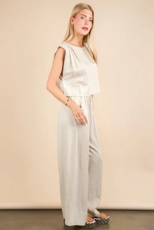 woman wearing a beige woven two-piece set with wide-leg pants and a sleeveless cropped top, styled for a chic minimalist look