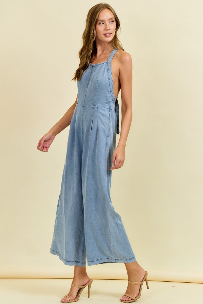 Woman wearing a blue denim jumpsuit against a beige background