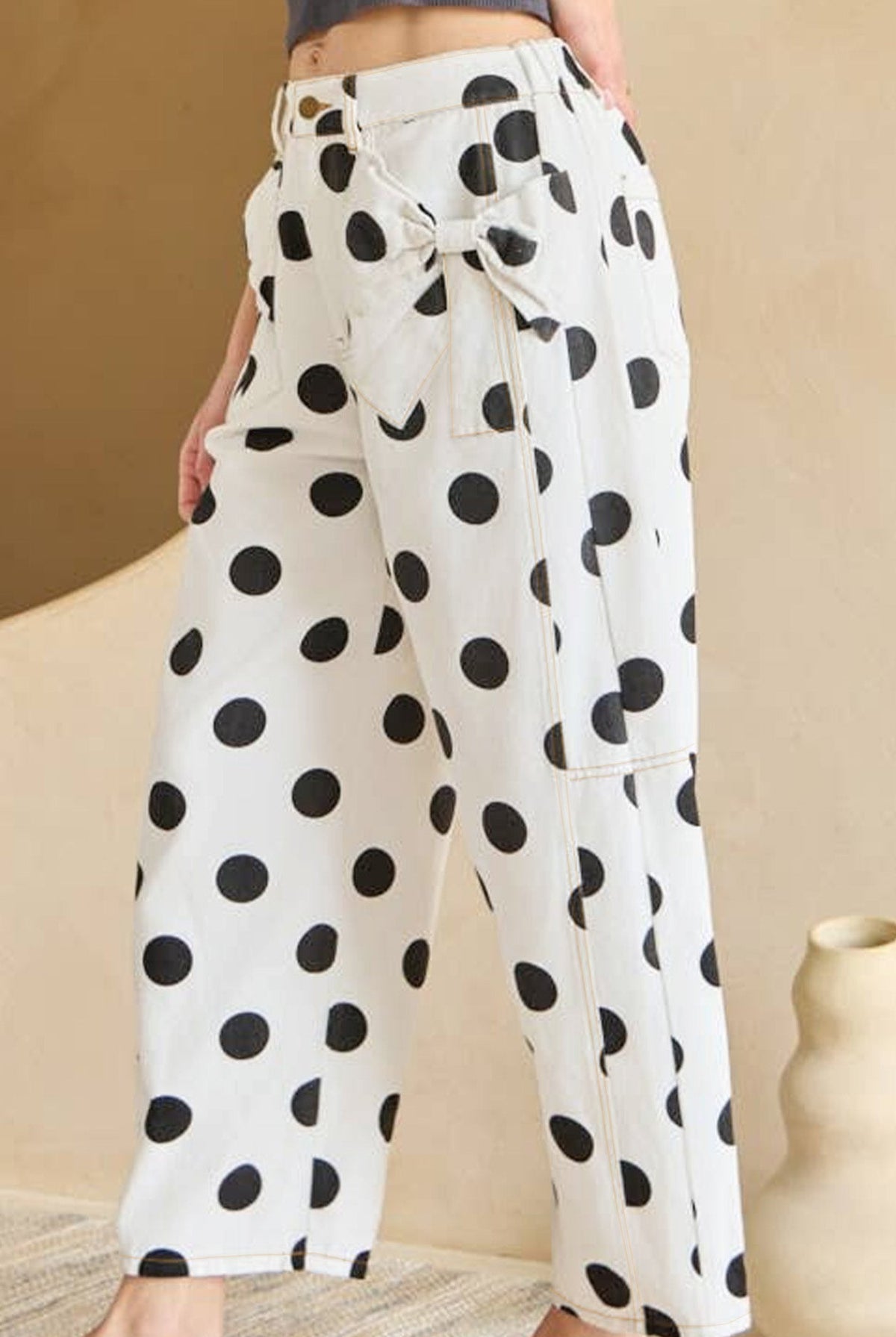 Person wearing white pants with black polka dots in a minimal indoor setting.