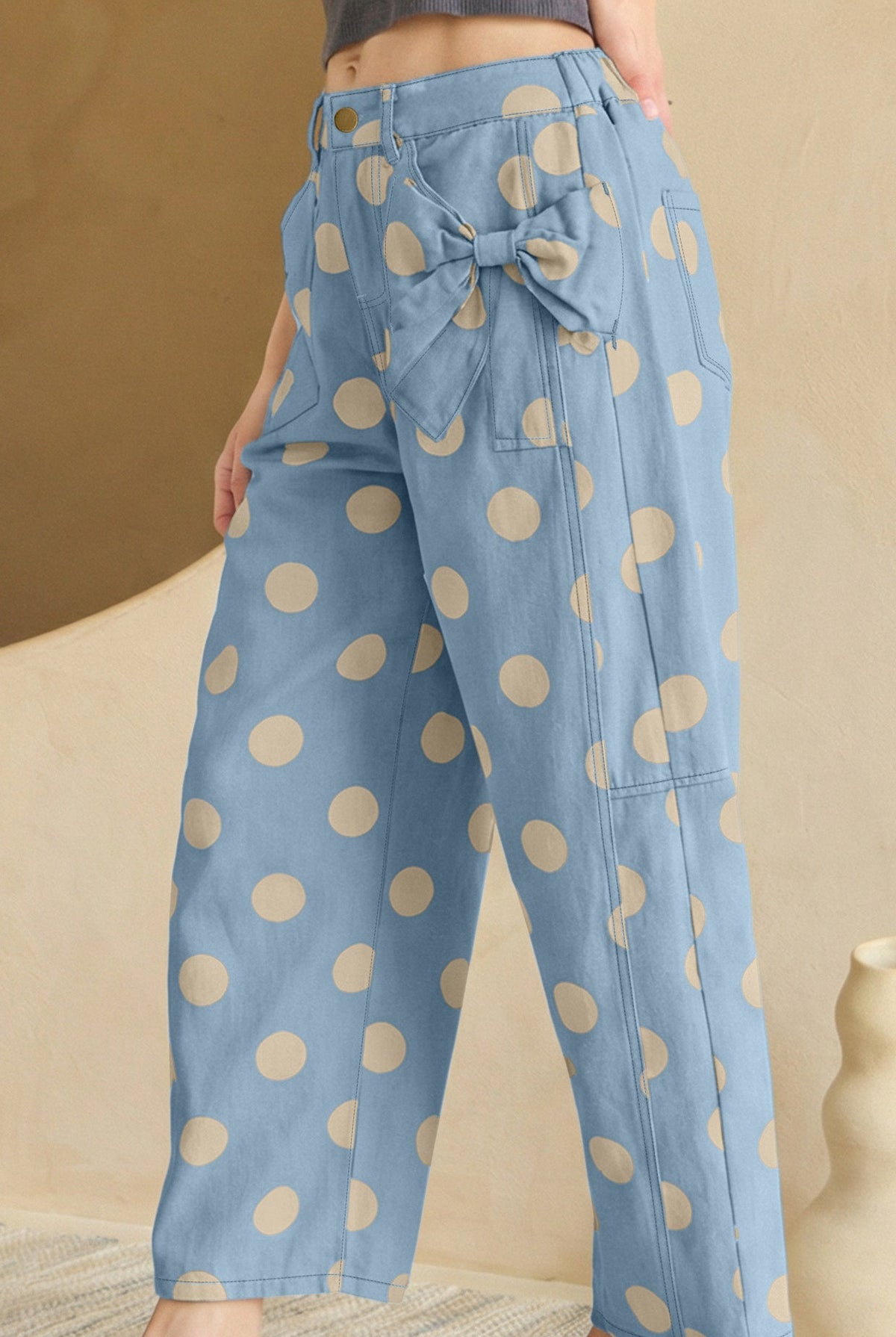 Blue pants with beige polka dots worn by a person, standing against a beige background.