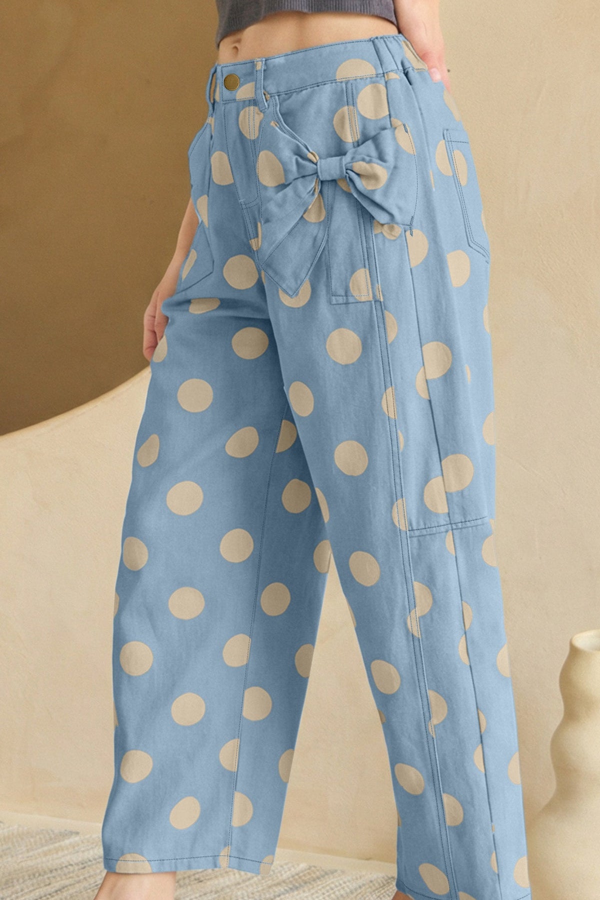 Blue pants with beige polka dots worn by a person, standing against a beige background.