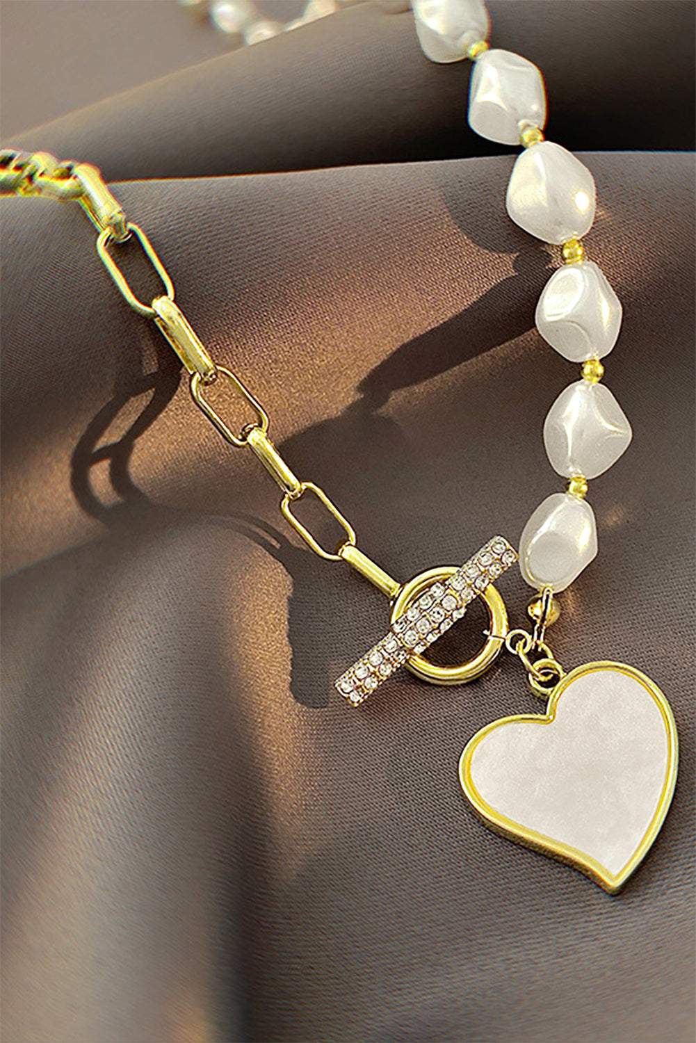 Pearl bracelet with gold chain and heart-shaped charm on a brown surface
