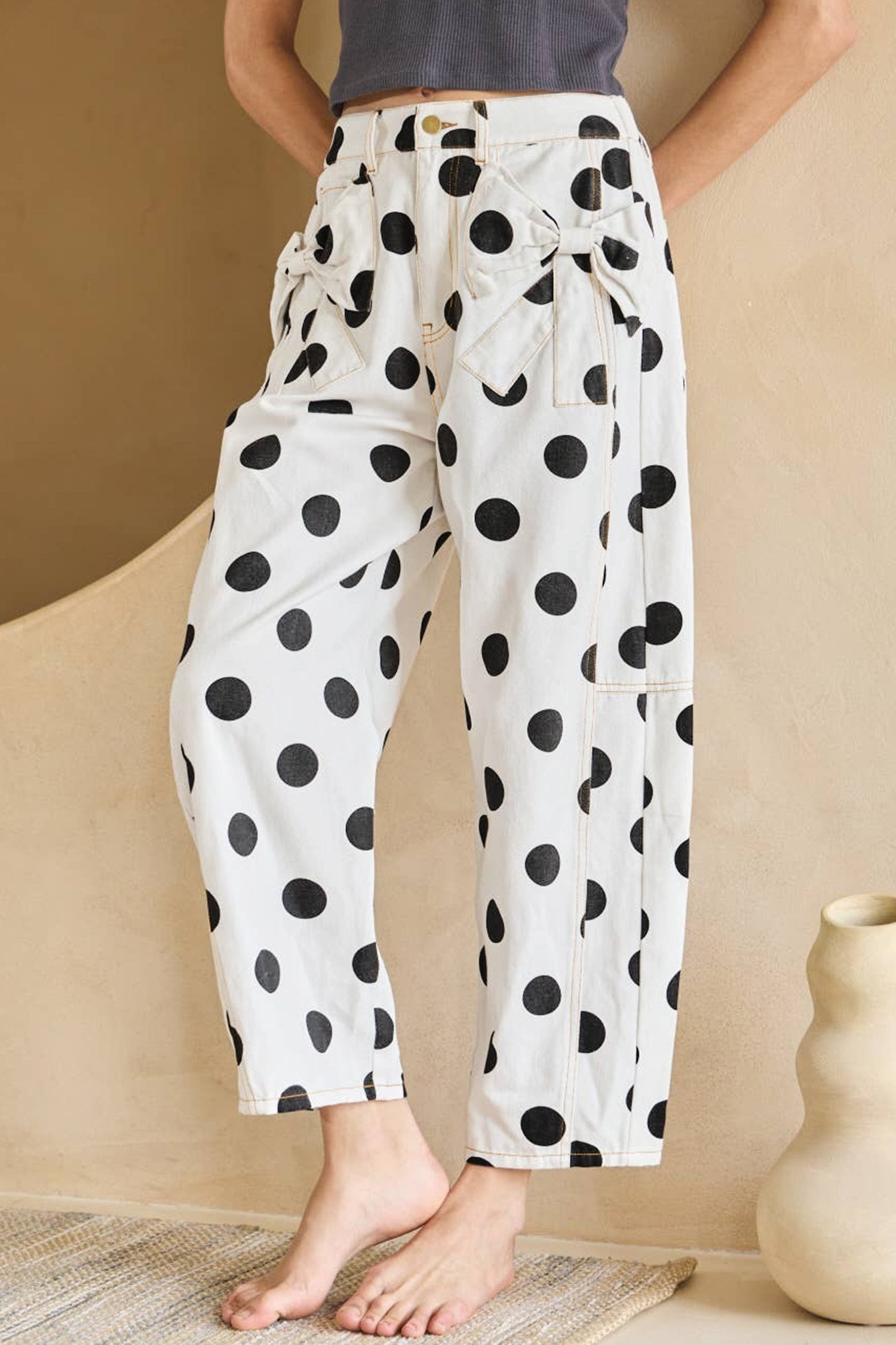Person wearing white pants with black polka dots in a minimal indoor setting.