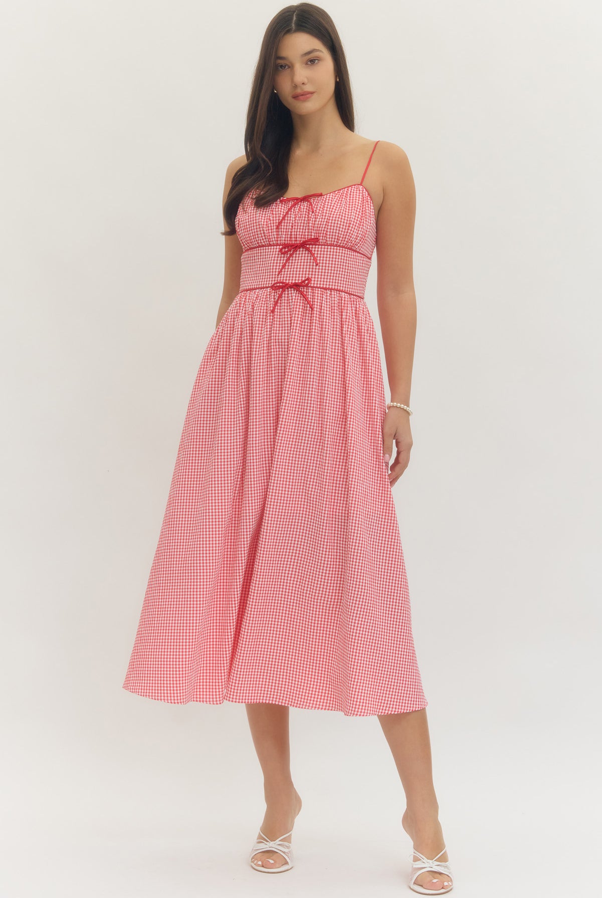 Model wearing a sweetheart gingham maxi dress with adjustable straps, bow details, smocked back, and side pockets in a romantic gingham print, perfect for Valentine’s Day and spring occasions.