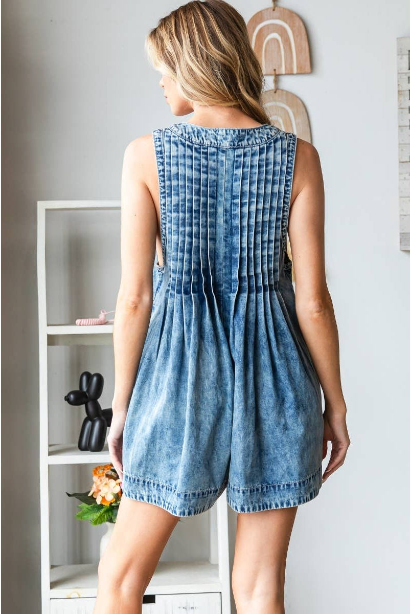 Woman wearing a stylish sleeveless denim romper with deep V-neckline, front pleats, and tie detail at the bust; perfect trendy summer outfit for women from a boutique collection.