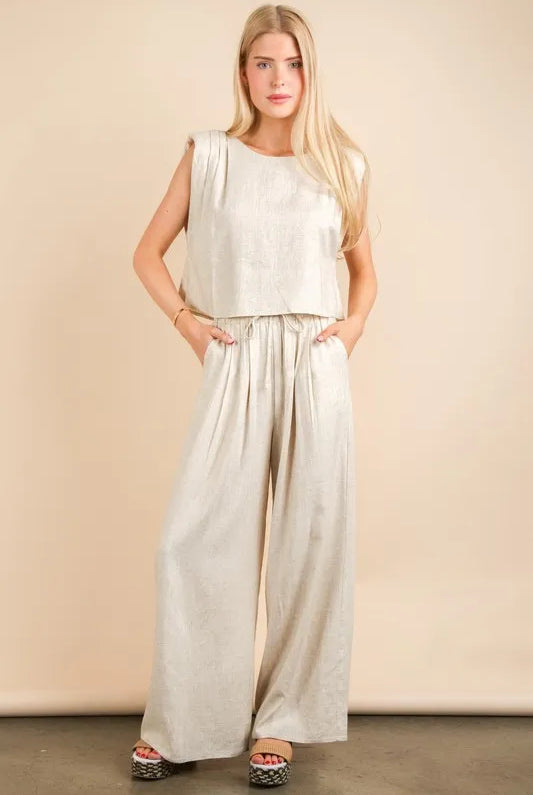 woman wearing a beige woven two-piece set with wide-leg pants and a sleeveless cropped top, styled for a chic minimalist look