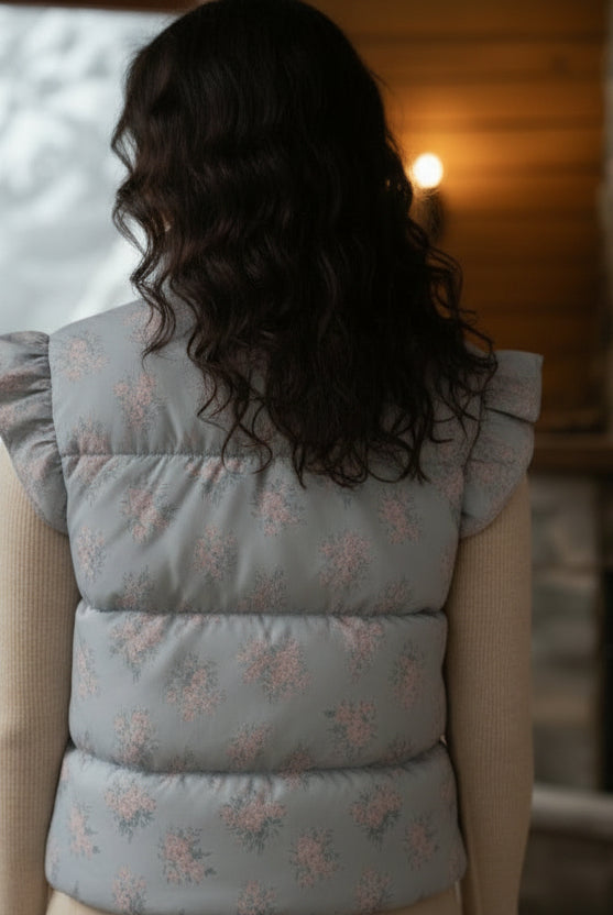 Woman wearing a light blue puffer vest with floral pattern in a cozy indoor setting.