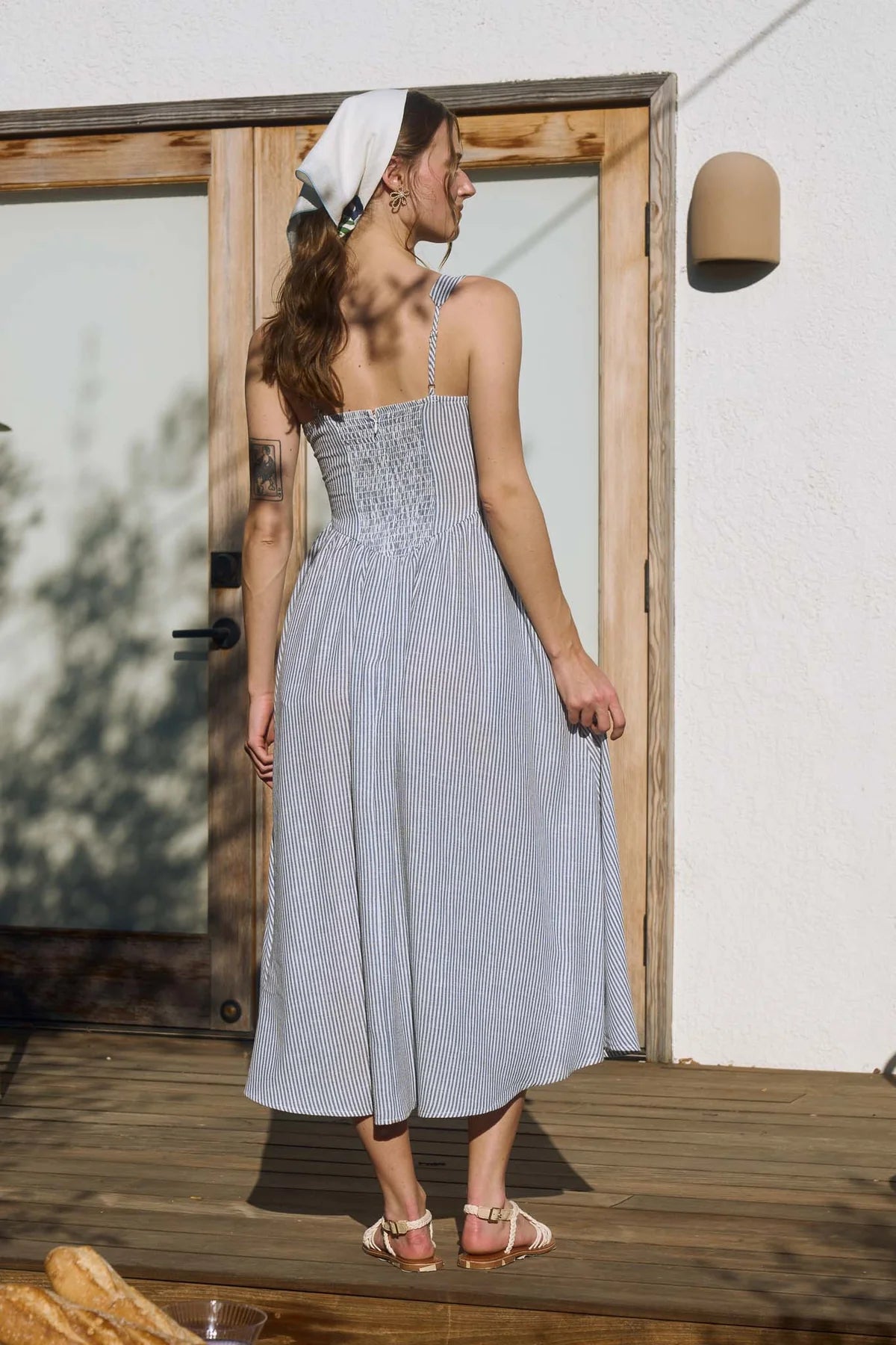 Rear view of a striped midi dress showcasing a functional smocked back dress panel for an adjustable fit. The taupe stripes remain continuous from the shoulder straps down to the hem of the A-line summer dress