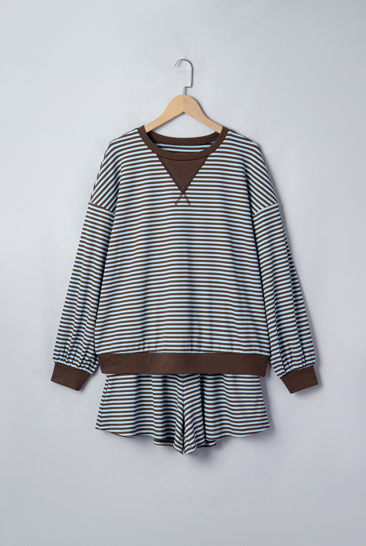 A long-sleeve striped top with brown ribbed trim, hanging on a wooden hanger against a light gray wall.