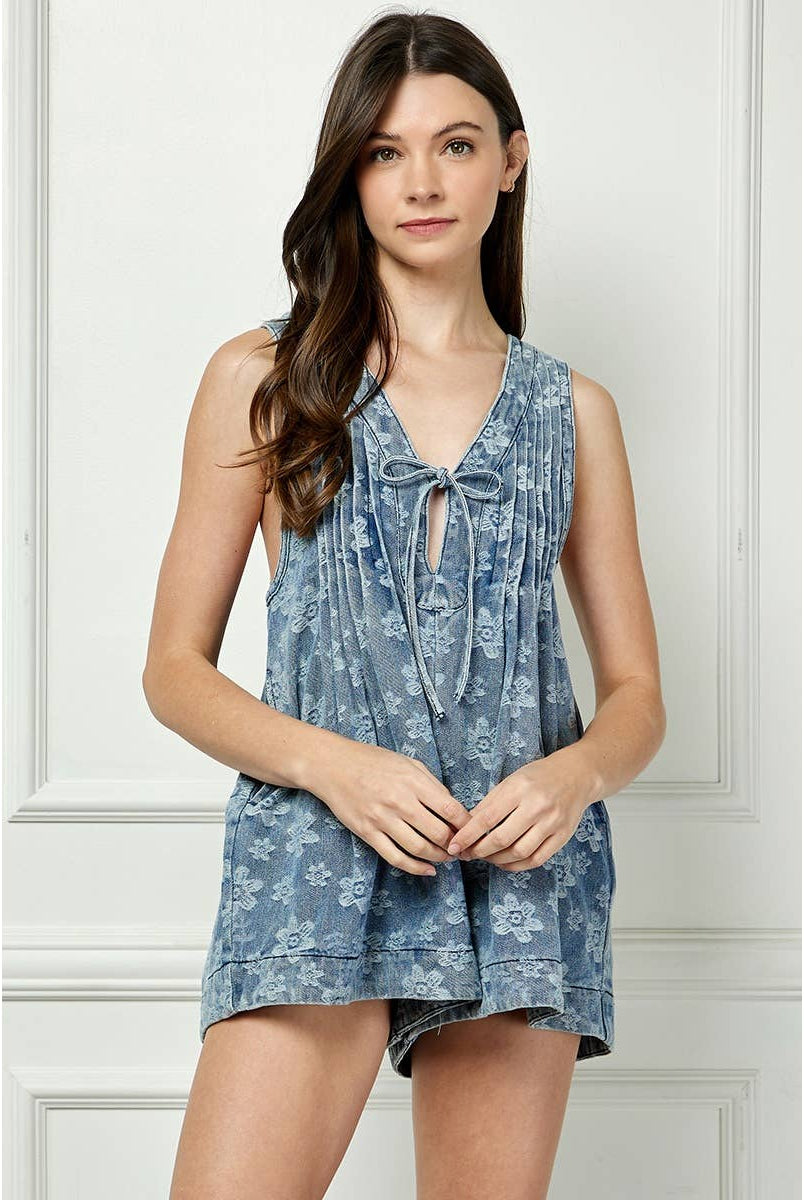 printed denim romper Model wearing the Skylar Tie Front Romper, a sleeveless floral-washed denim romper with pleated front and keyhole tie neckline