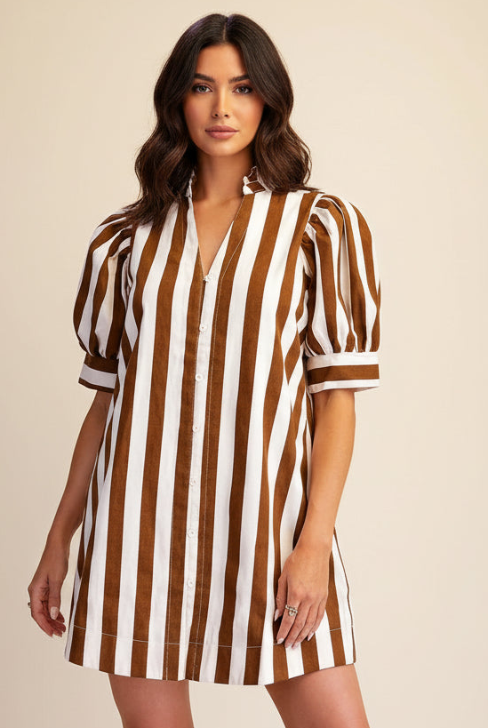A woman modeling a brown and white vertically striped short-sleeve button-up dress with puff sleeves, photographed against a plain beige studio background.
