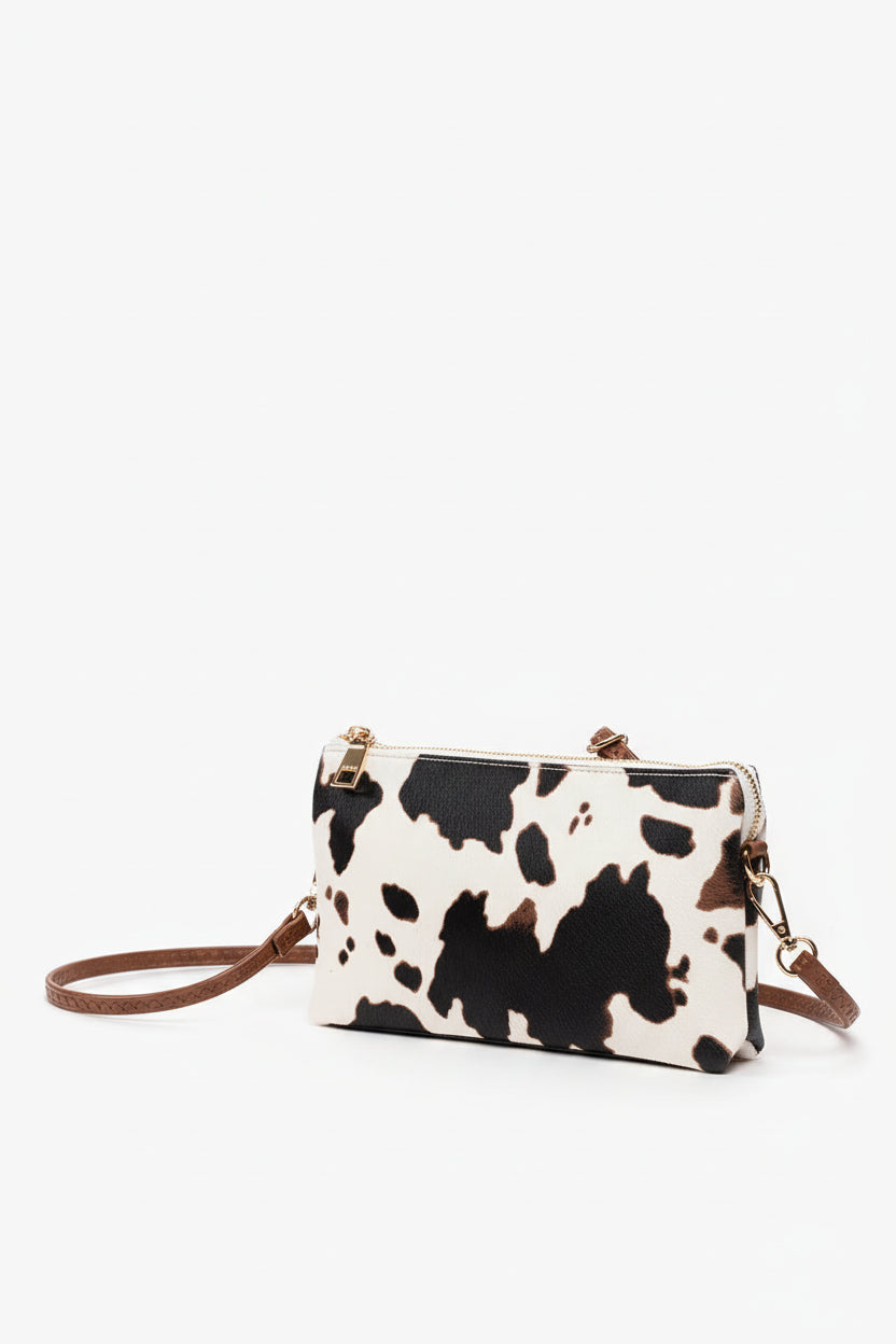 Cow print handbag with brown strap on a white background