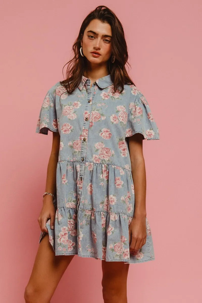 Model wearing the Wild Rose Shirt Dress in soft blue with rose print, flutter sleeves, and tiered ruffle skirt