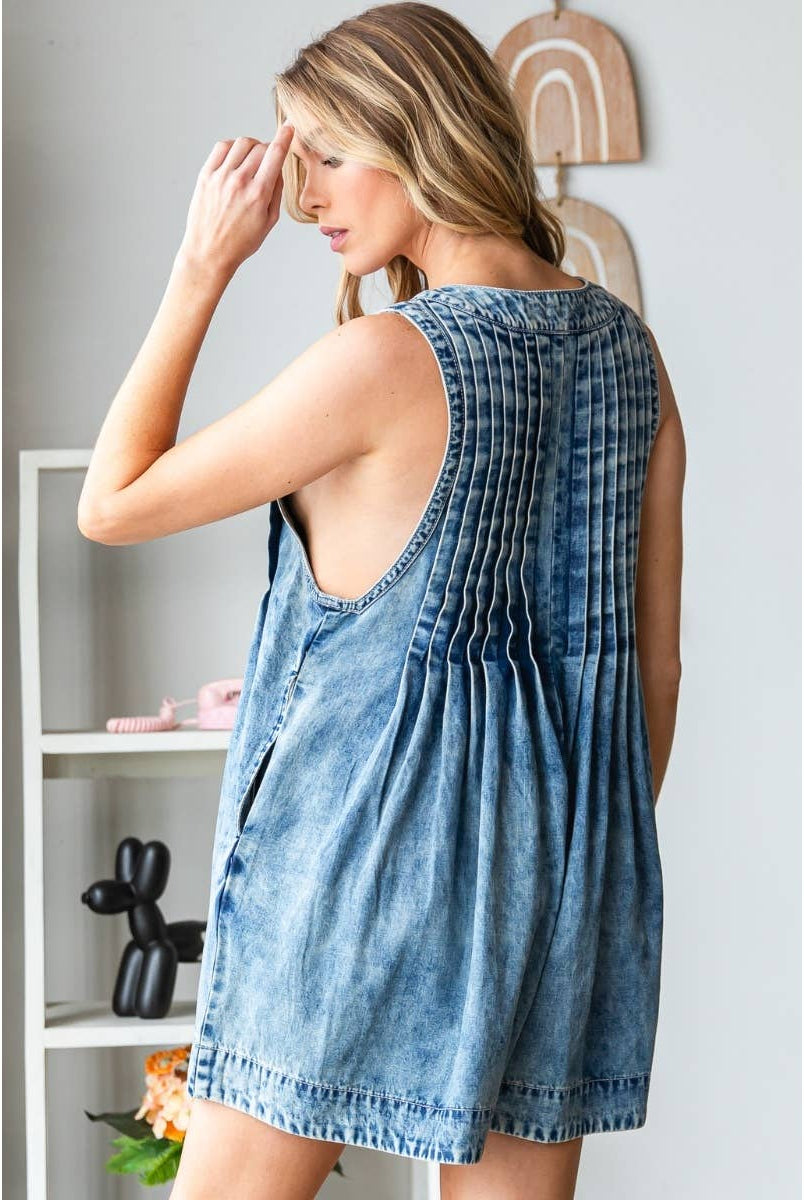 Woman wearing a stylish sleeveless denim romper with deep V-neckline, front pleats, and tie detail at the bust; perfect trendy summer outfit for women from a boutique collection.