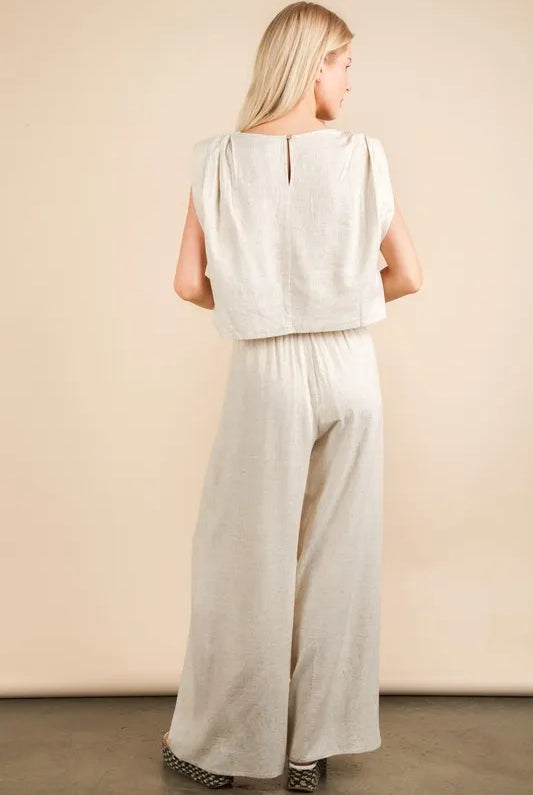 woman wearing a beige woven two-piece set with wide-leg pants and a sleeveless cropped top, styled for a chic minimalist look