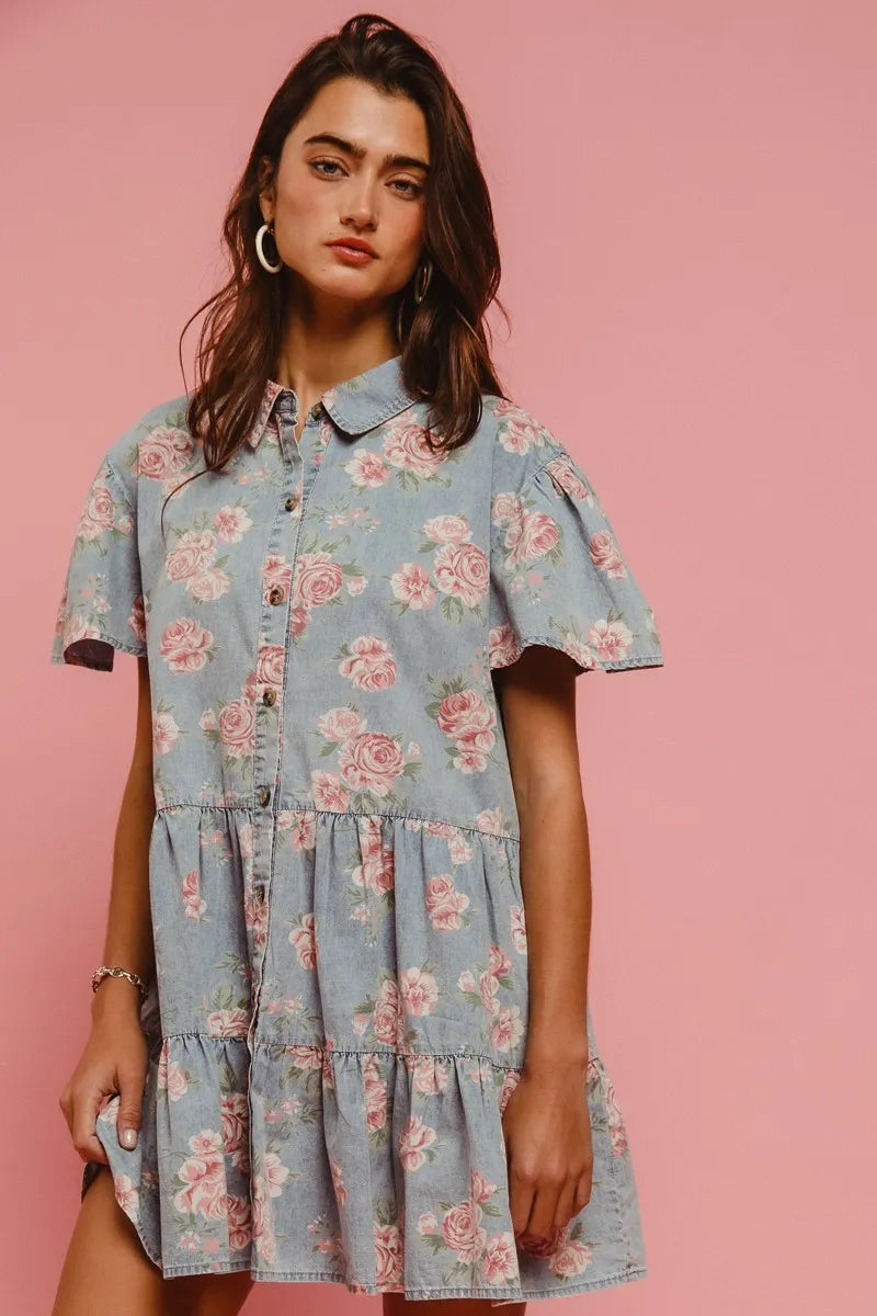 Model wearing the Wild Rose Shirt Dress in soft blue with rose print, flutter sleeves, and tiered ruffle skirt