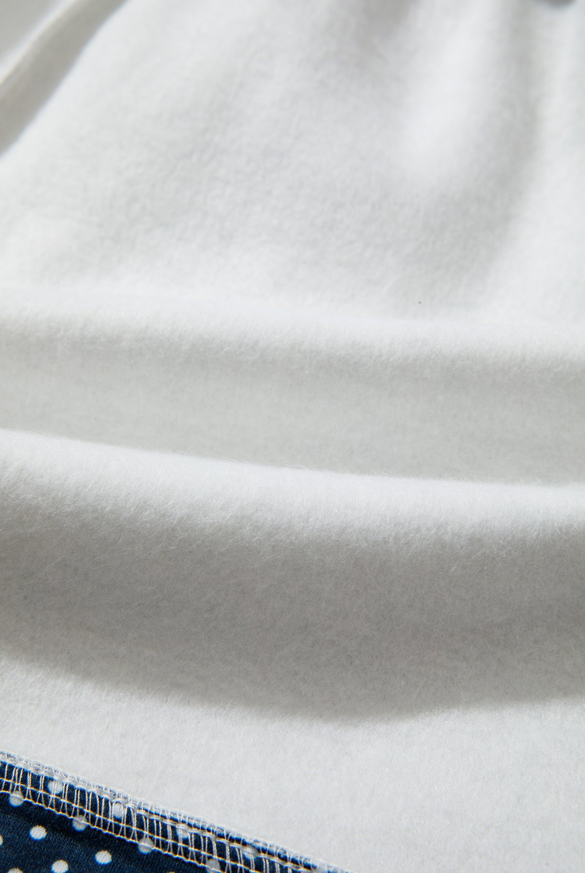 A close-up of a white textured fabric, likely fleece or sherpa, with soft folds and a small portion of a blue patterned textile visible at the bottom edge.