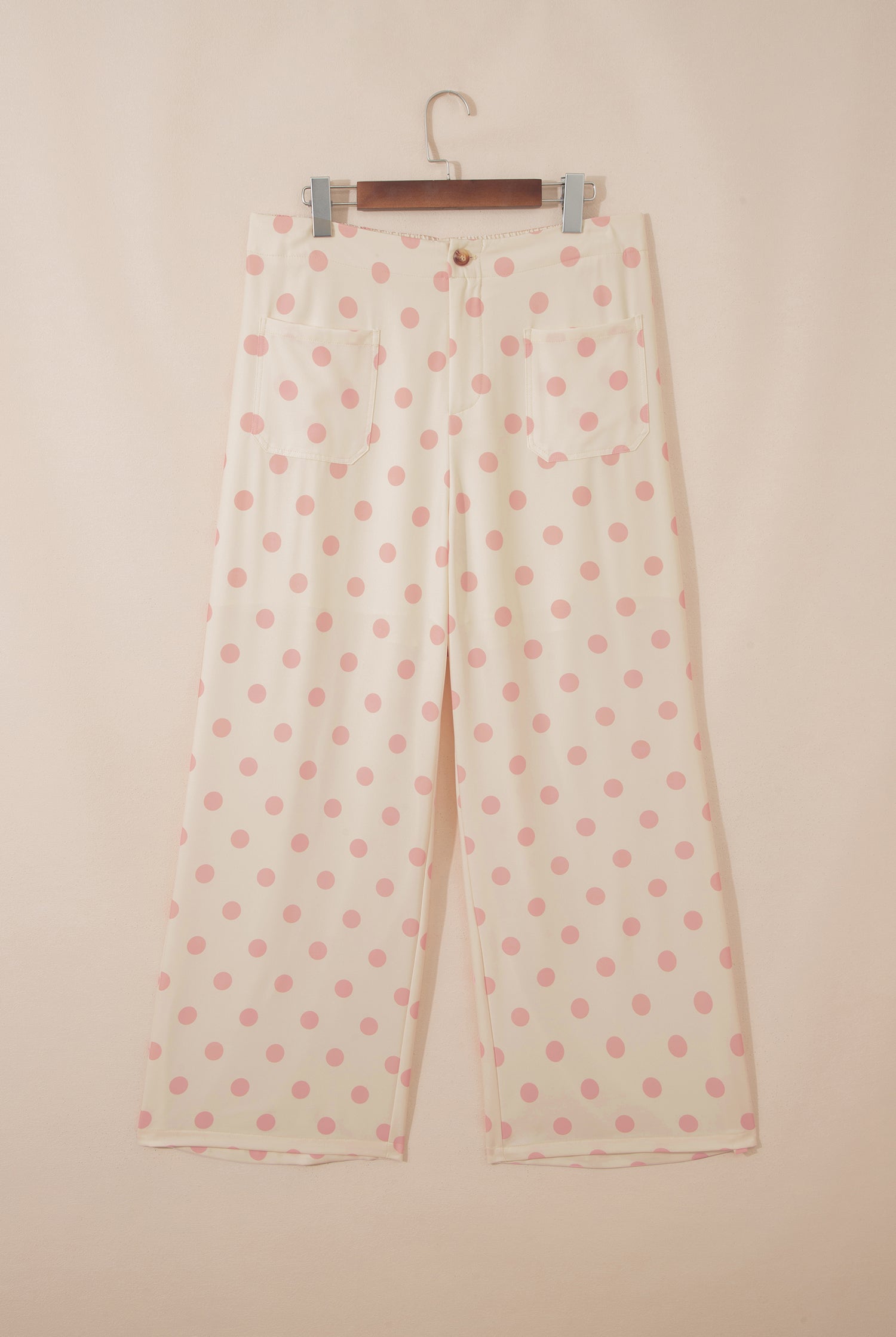 Polka dot pants on a hanger against a beige background