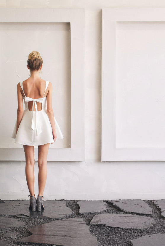 Sleeveless white square neck mini dress with open back tie detail and structured bodice