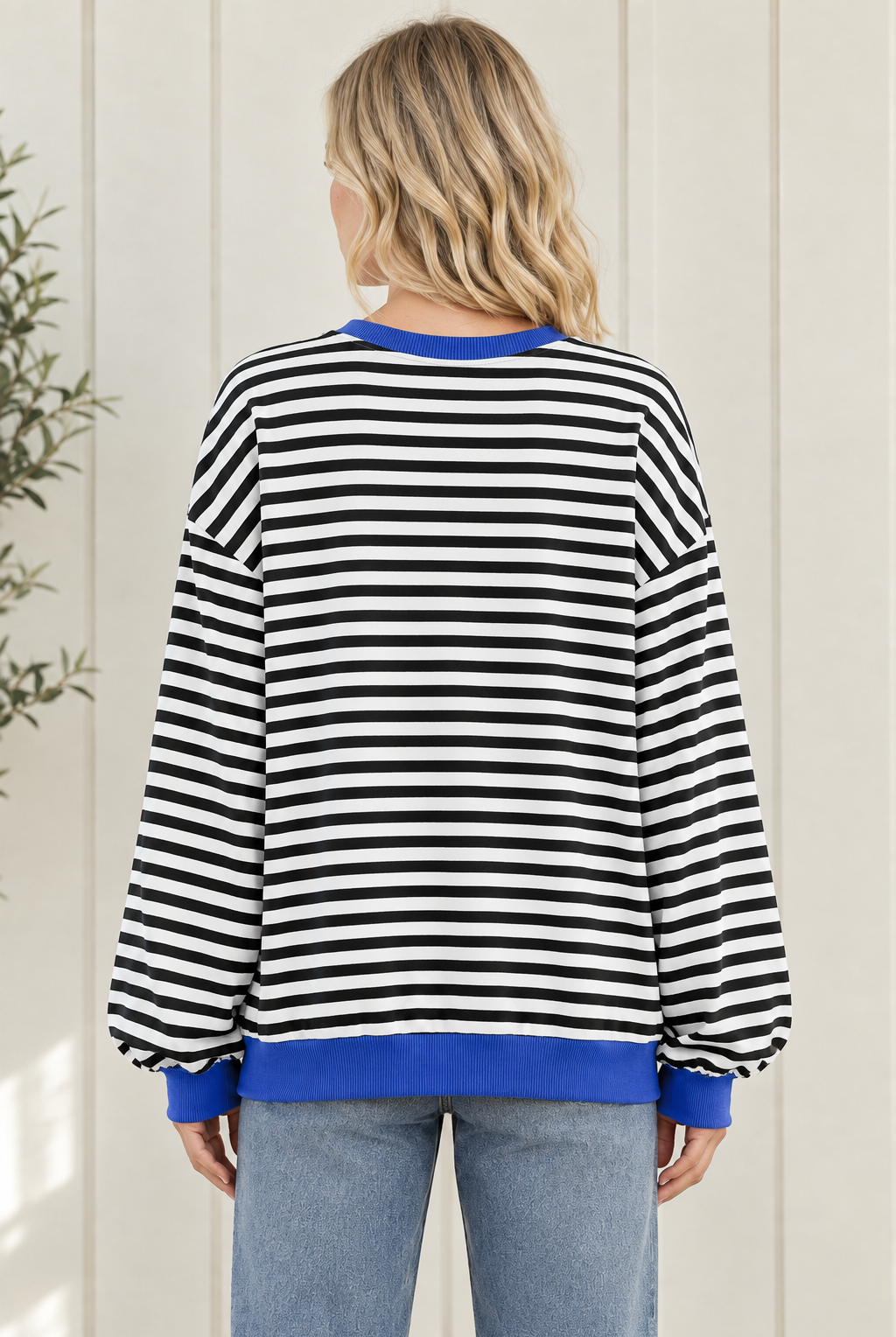Back view of women's black and white striped sweatshirt showing oversized fit, long sleeves and blue ribbed hem.