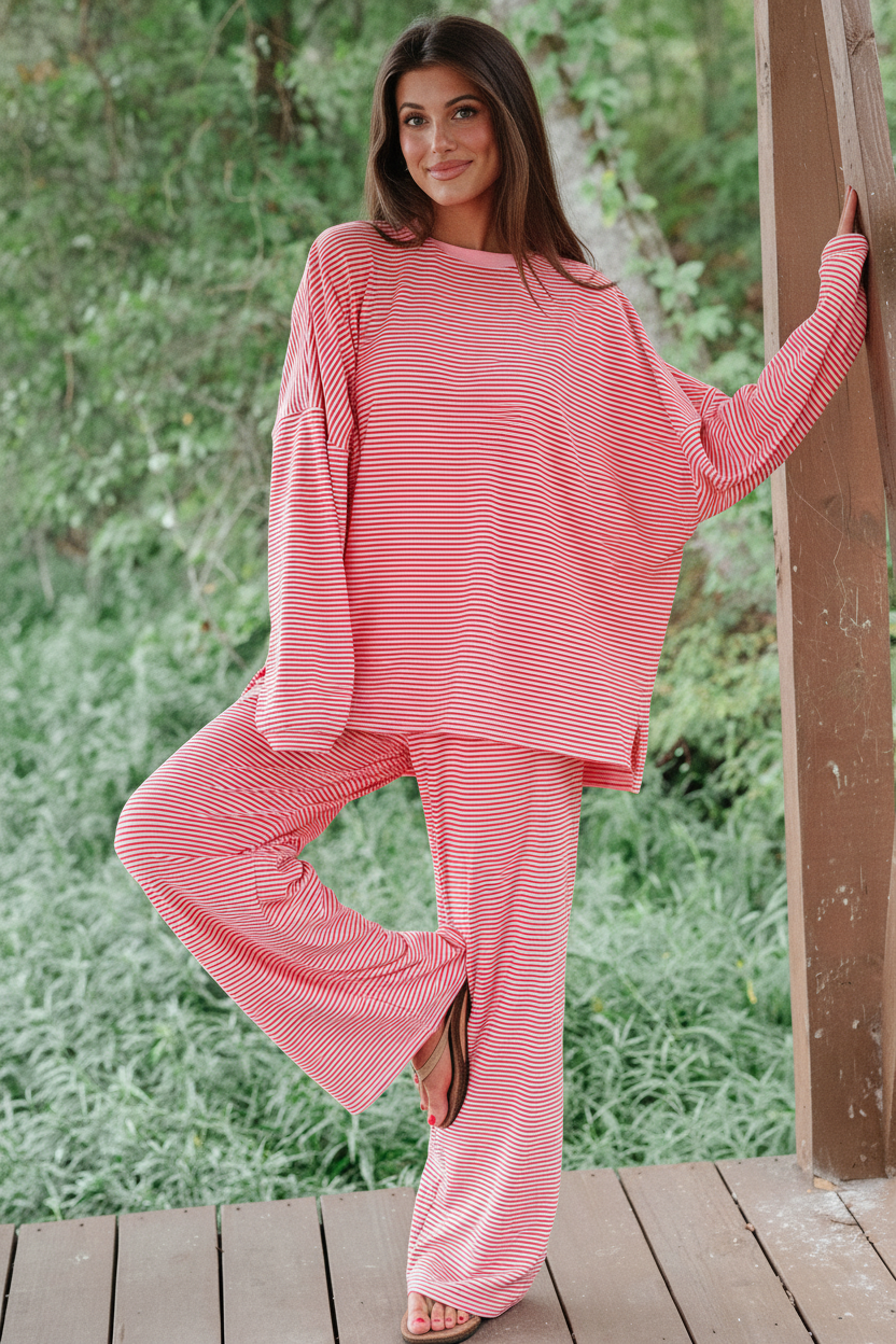 Model wearing red white stripe oversized drop shoulder pullover and wide-leg pants - front pose leaning on wooden post outdoors