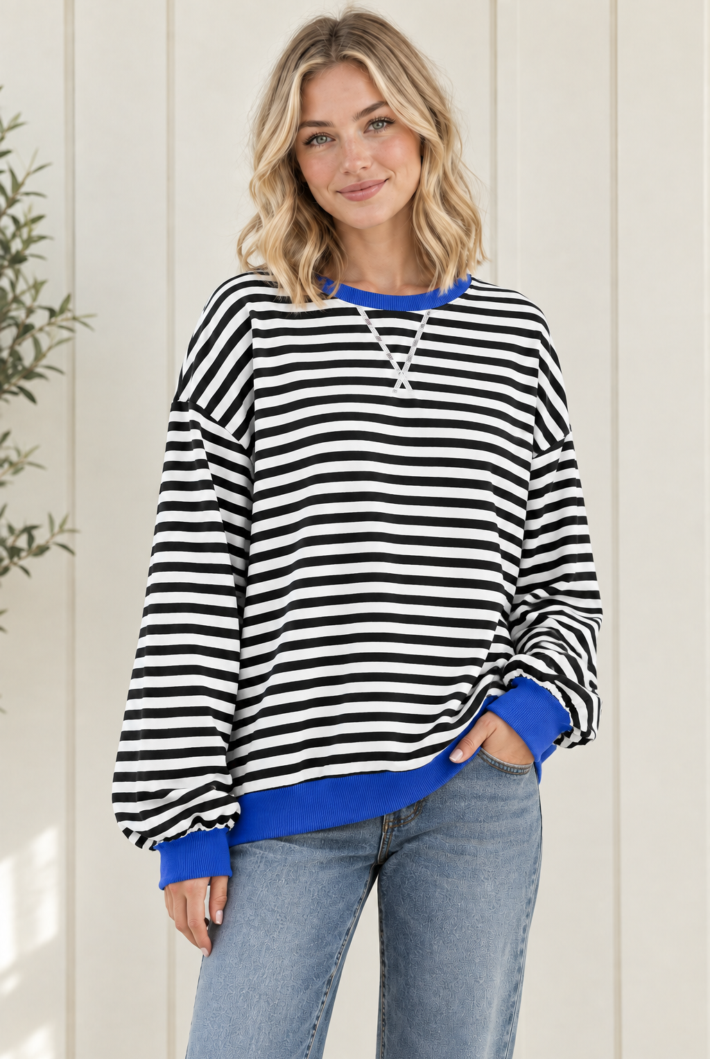 Three quarter view of oversized striped pullover sweatshirt with blue neckline, cuffs and hem, styled with jeans.