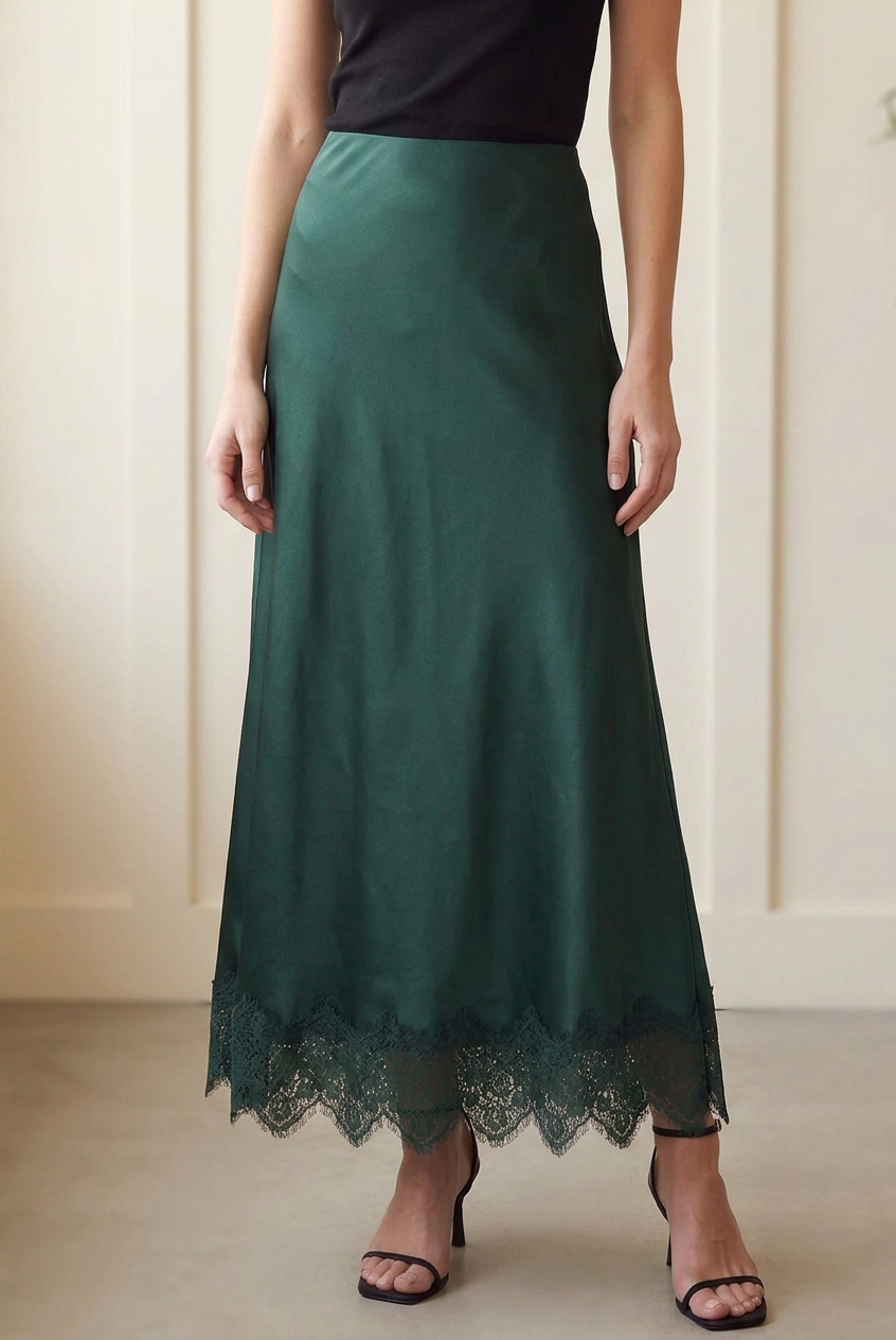Detail of forest green woven satin maxi skirt showing the lustrous fabric and scalloped floral lace trim.