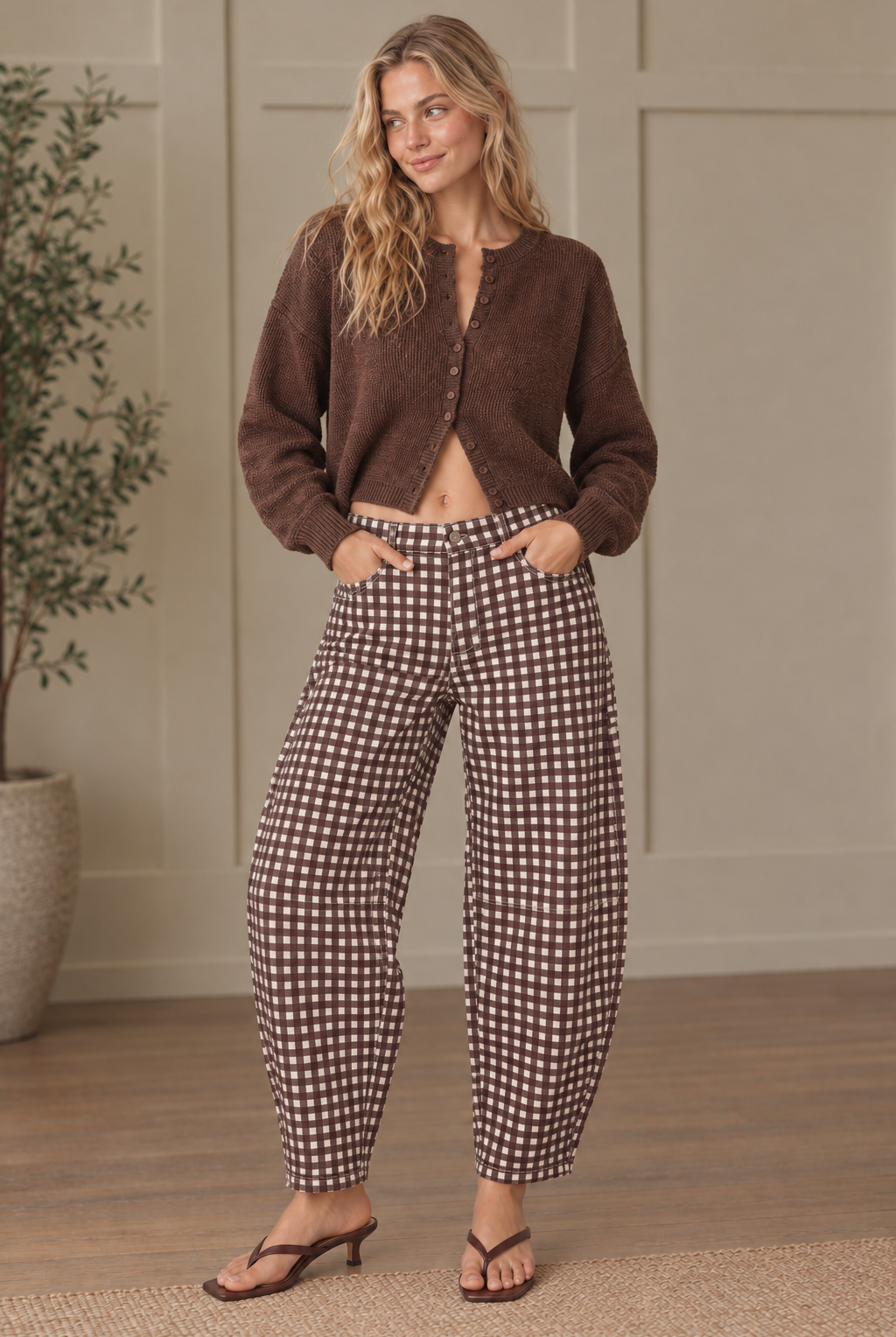 Brown gingham barrel-leg pants with hands in front pockets, showing rounded legs, belt loops and tapered ankle hems.