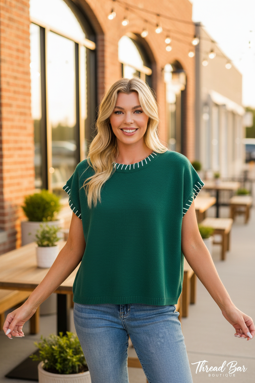 Hunter green short sleeve oversized sweater front view showing white whipstitch detailing along neckline and sleeve edges, relaxed fit styled with denim jeans
