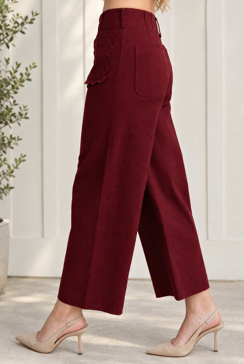 Side and rear view of burgundy cropped wide leg pants showing a plain back patch pocket and scalloped front pocket.