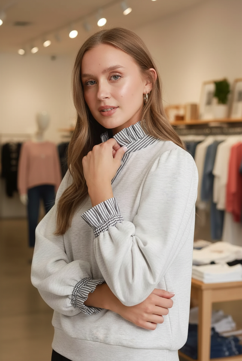 Close-up of a blonde woman wearing the Umgee heather white sweatshirt top showing the contrast navy and white vertical stripe ruffle collar and smocked ruffle stripe cuffs detail with gold hoop earrings