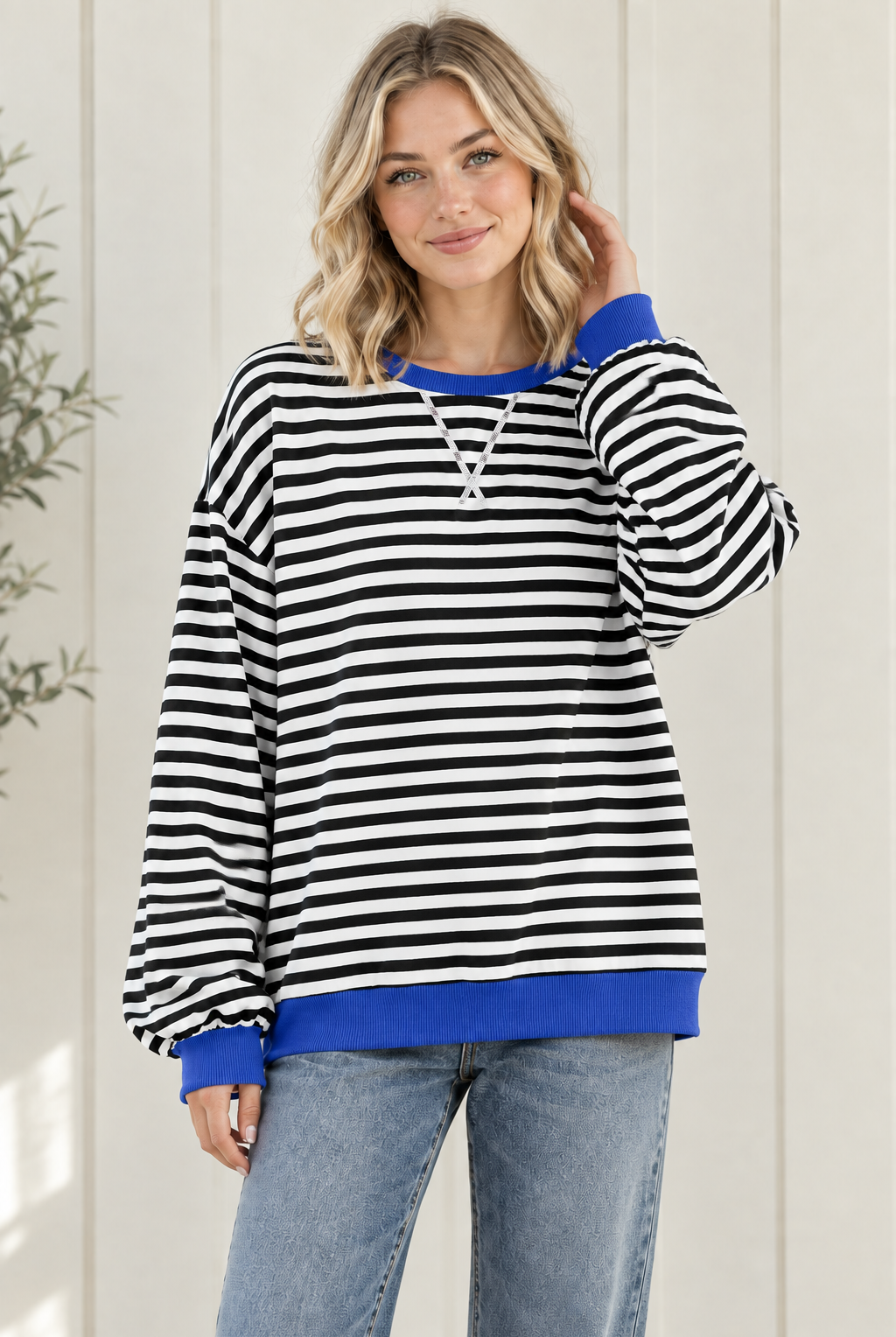 Women's oversized black and white striped sweatshirt with blue ribbed trim and drop shoulders, styled with jeans in a relaxed front pose.