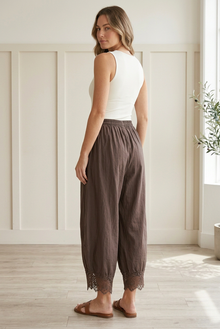 Rear three-quarter view of chocolate brown woven barrel pants with roomy curved legs, cropped length, and scalloped floral lace hems.