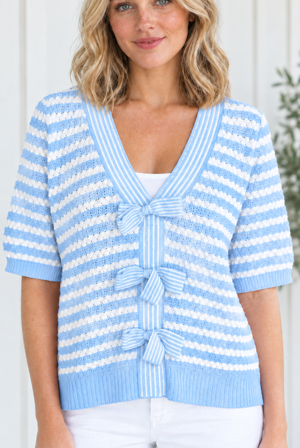 Close-up of sky blue and white textured knit stripes, V-neck trim and three striped bow ties on sweater front