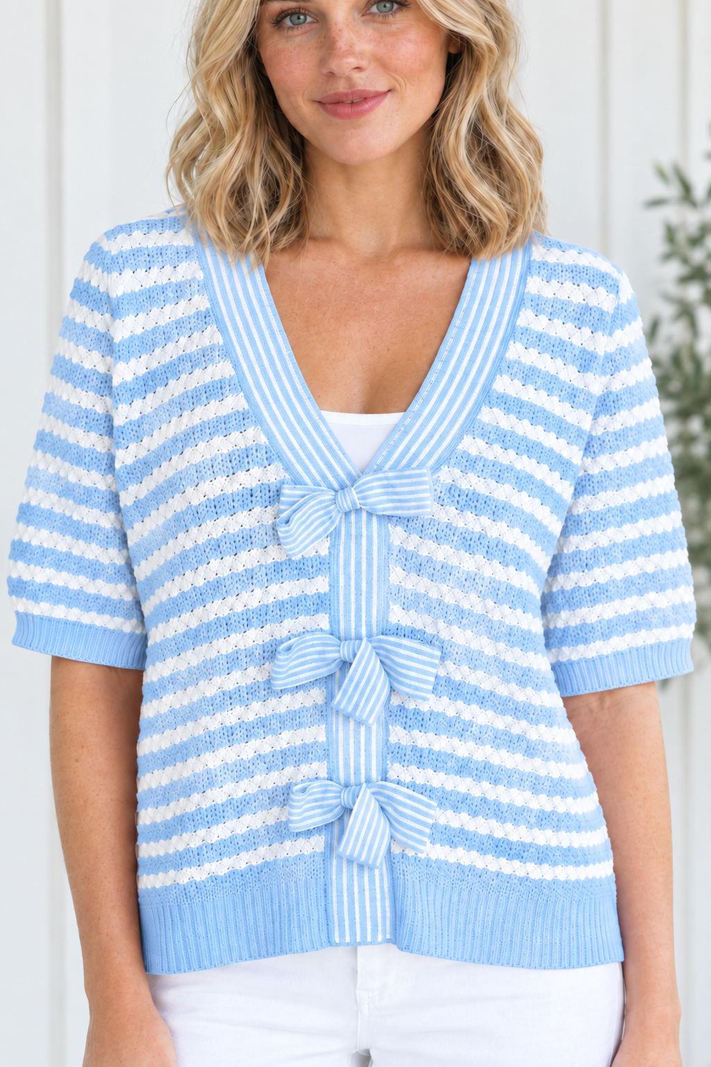 Close-up of sky blue and white textured knit stripes, V-neck trim and three striped bow ties on sweater front