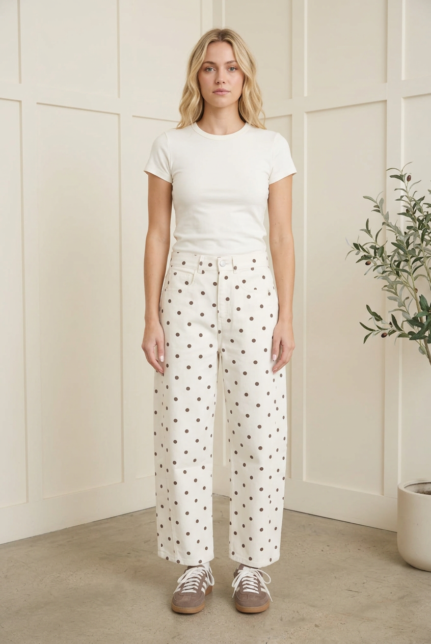 Front styling view of ecru high waist barrel leg jeans with dark polka dots, an ivory tee and retro sneakers.