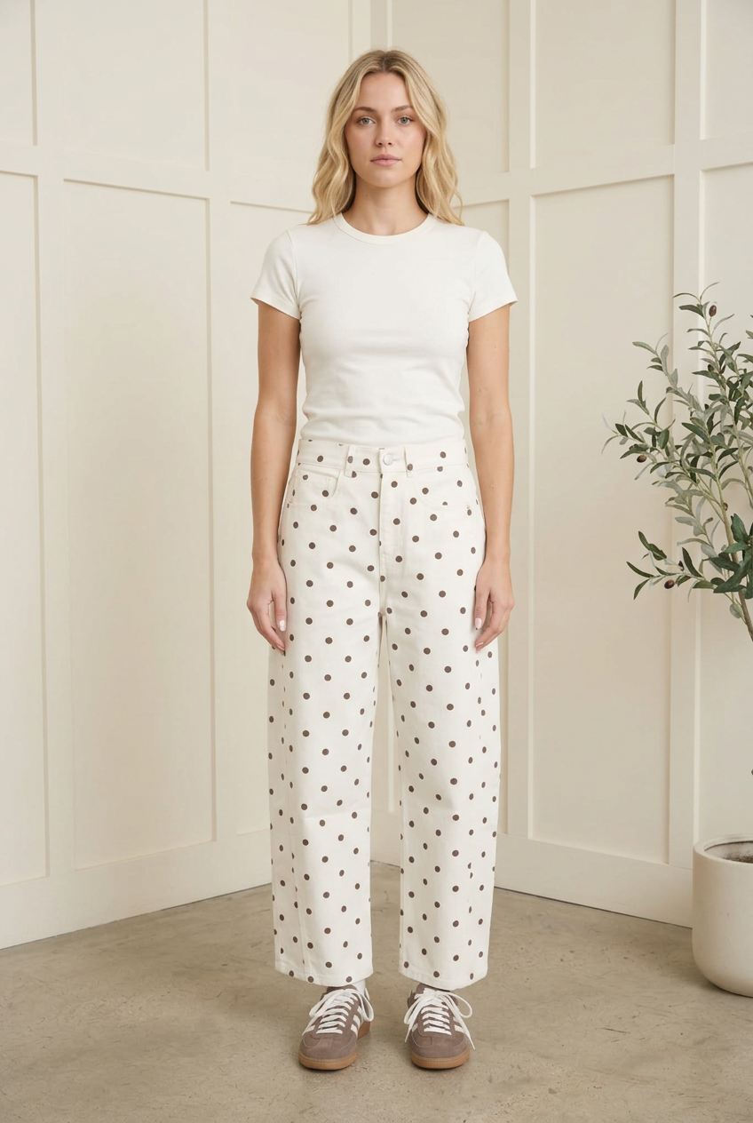 Front styling view of ecru high waist barrel leg jeans with dark polka dots, an ivory tee and retro sneakers.