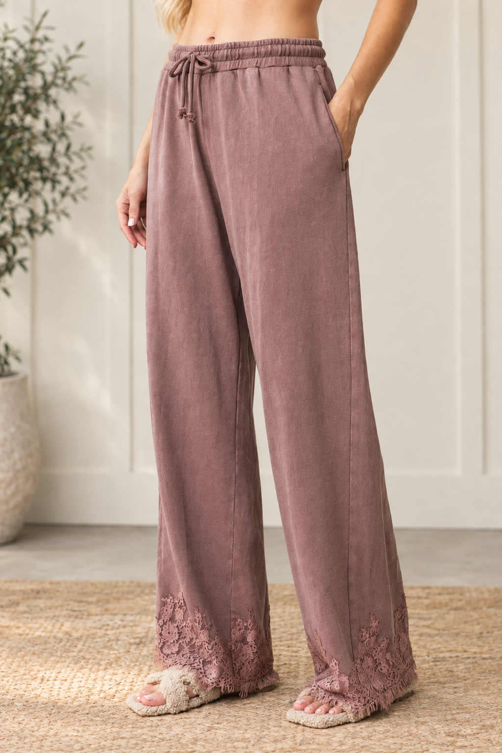 Angled view of mauve-brown French terry track pants showing side pockets, a relaxed wide-leg fit and floral lace hems.