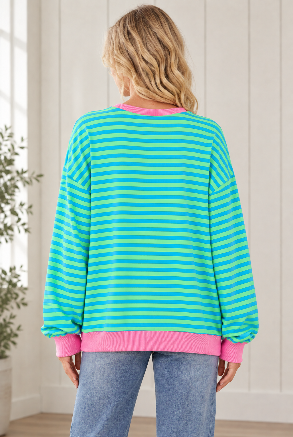 Back view of oversized blue and green striped pullover showing long sleeves and a pink ribbed hem.