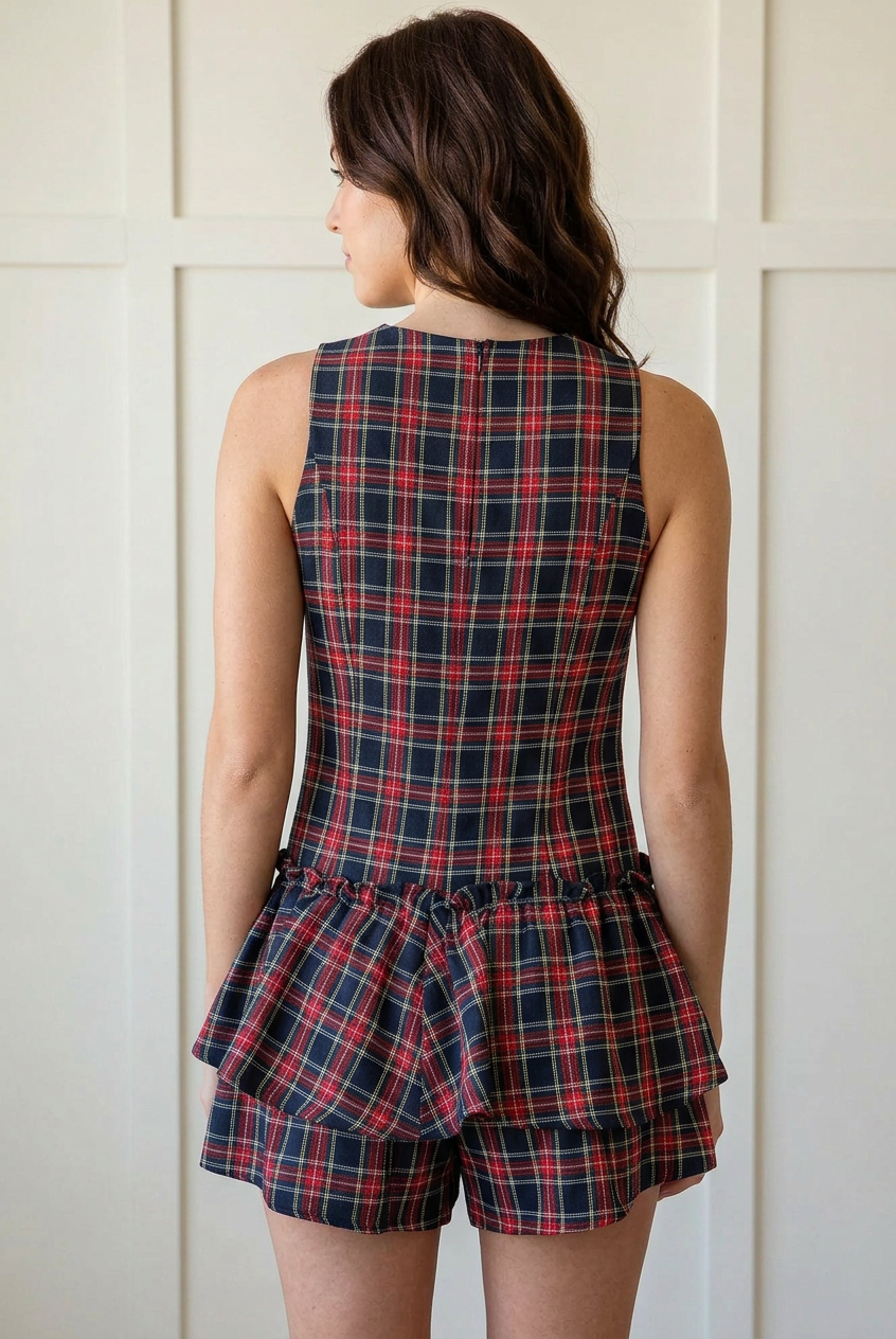 Back view of the sleeveless tartan plaid romper showing the fitted bodice, low gathered waist, and layered ruffles over shorts.