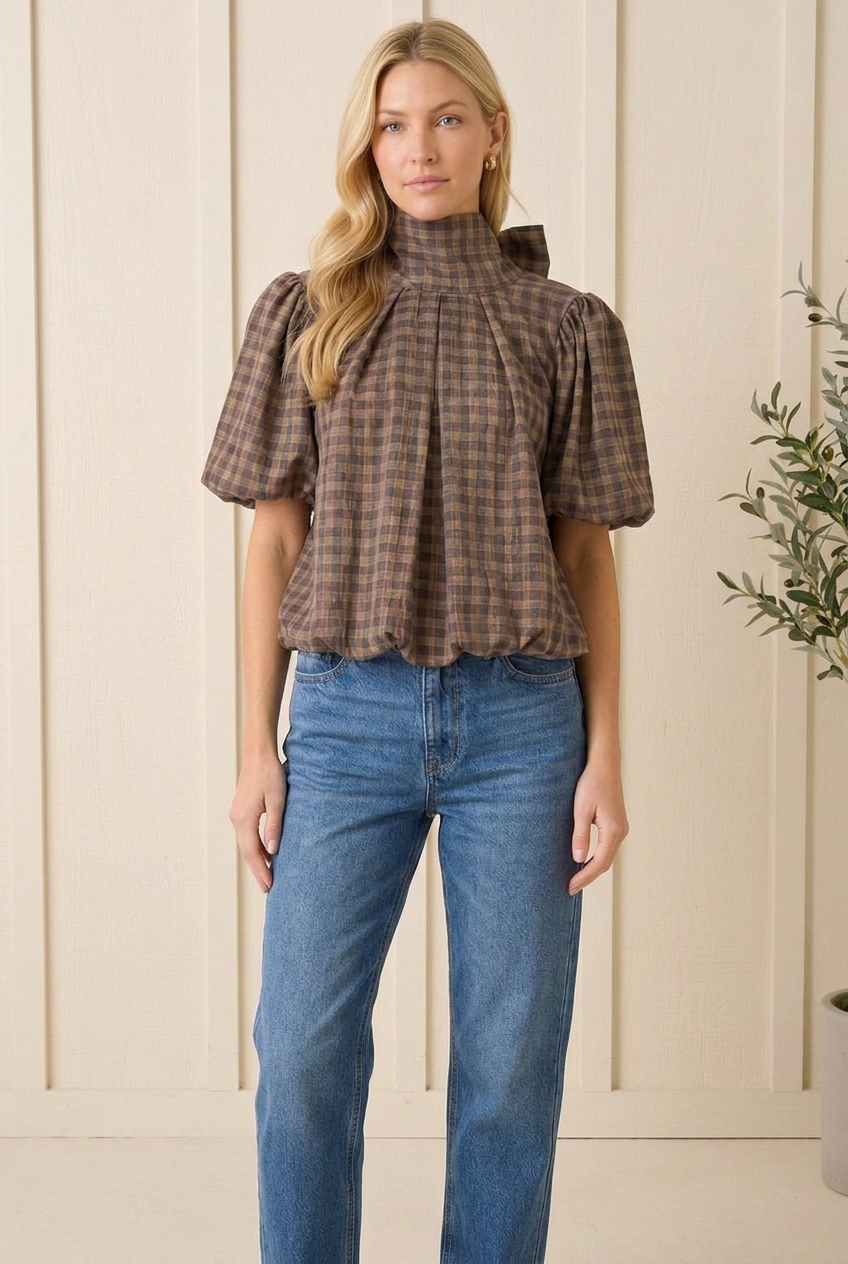 Front view of Entro brown gingham blouse with a high tie neckline, front pleats and gathered hem.
