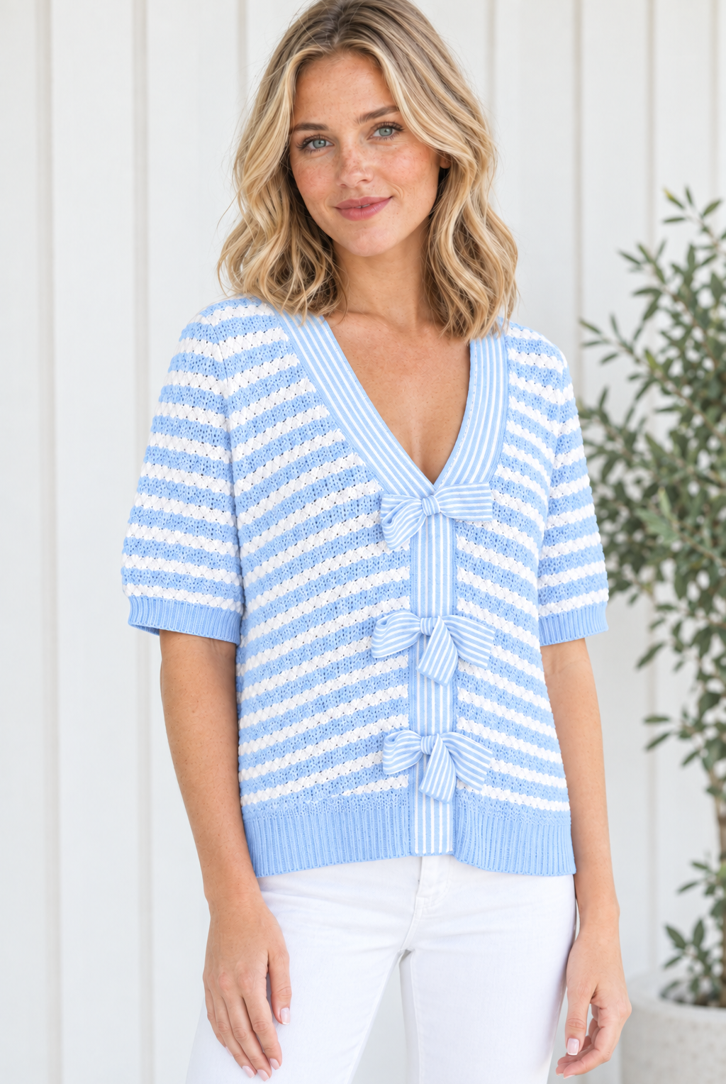Three-quarter view of women's sky blue striped knit sweater with short sleeves, V neckline and striped front bows