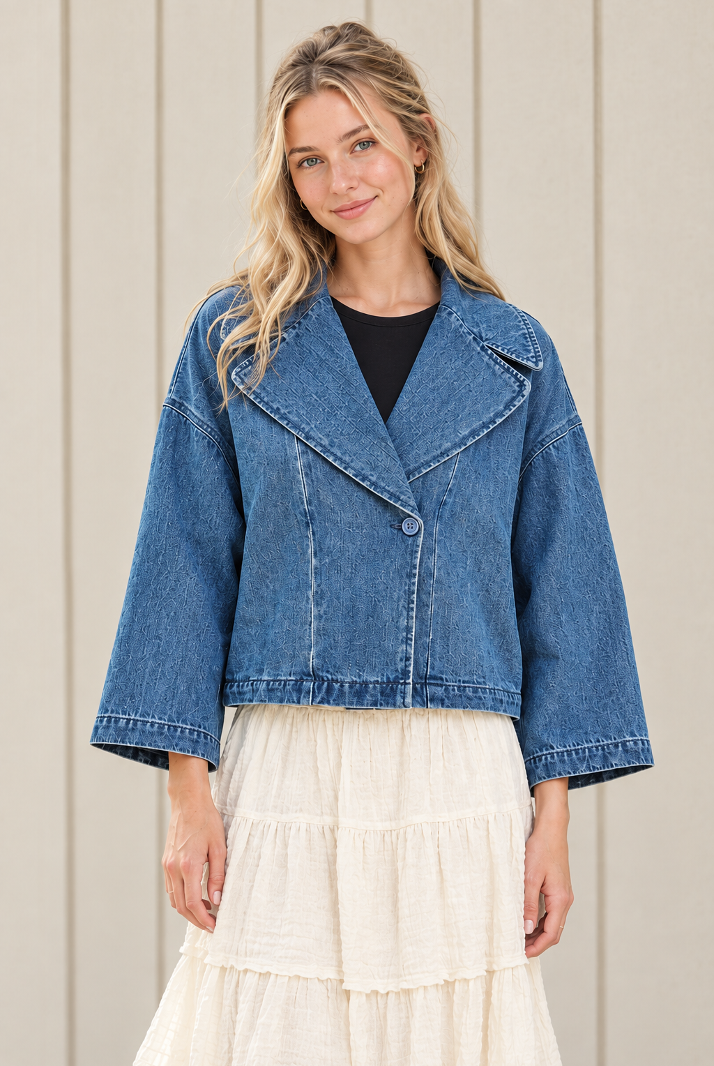 Front view of a blue boxy cropped denim jacket showing its single button closure, broad collar, dropped shoulders and stitched hem.