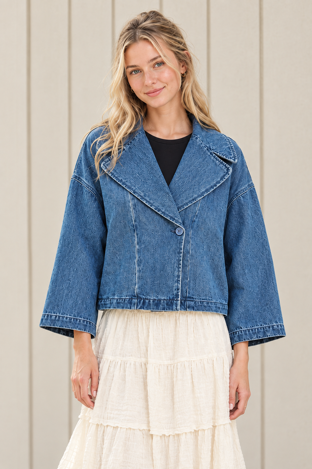 Front view of a blue boxy cropped denim jacket showing its single button closure, broad collar, dropped shoulders and stitched hem.