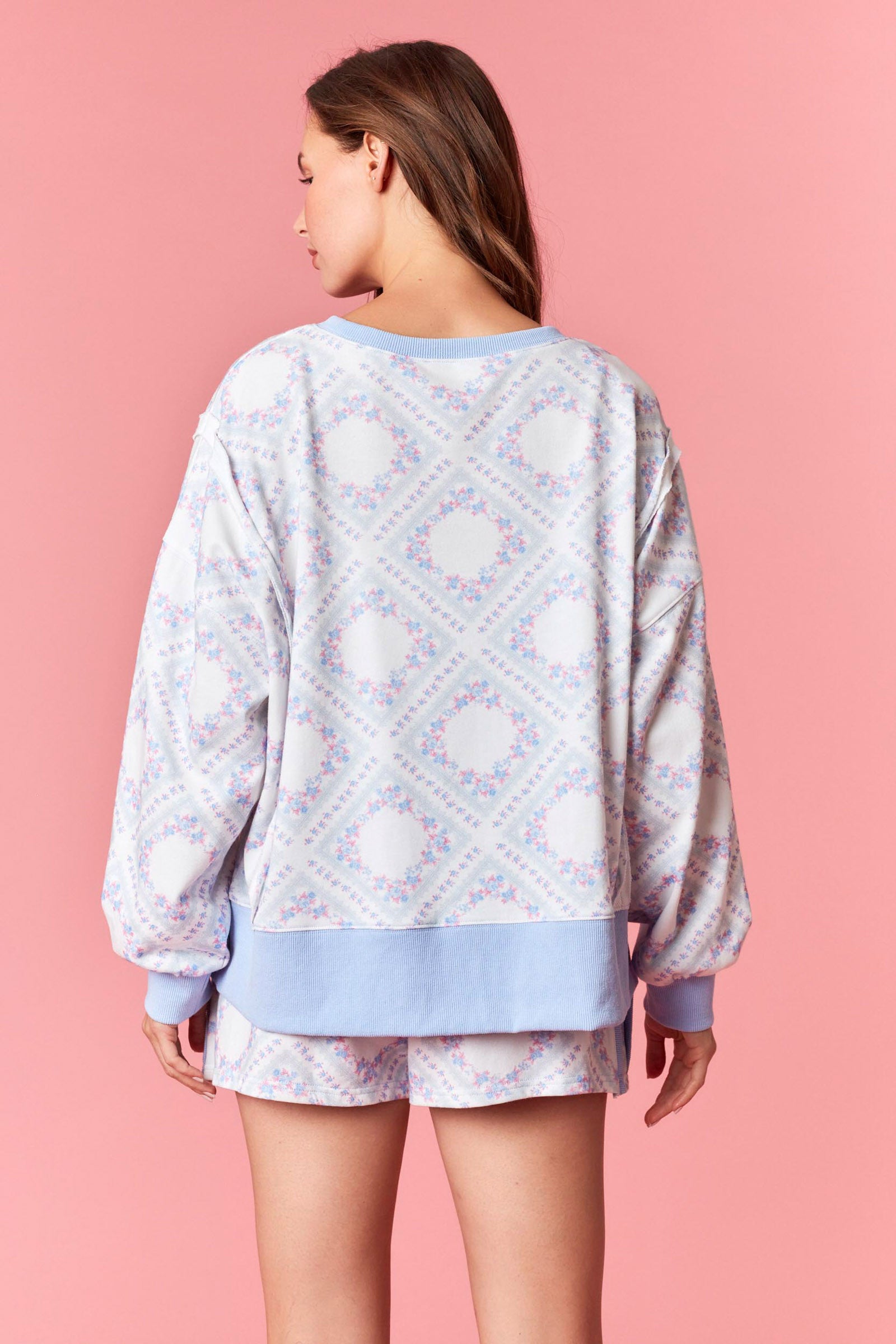 Woman wearing a pink and blue pastel floral printed French terry sweatshirt with ribbed trim, part of a matching lounge set