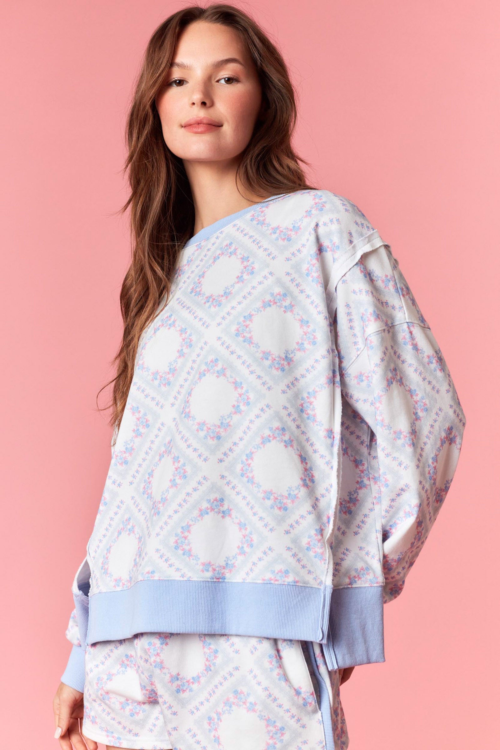 Woman wearing a pink and blue pastel floral printed French terry sweatshirt with ribbed trim, part of a matching lounge set