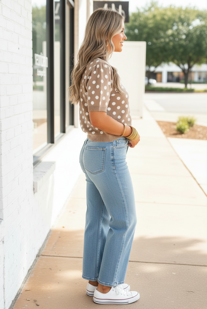 Side profile of blonde woman on sidewalk wearing taupe brown polka dot knit cardigan with white dots, ribbed cuffs and hem, paired with wide-leg light wash jeans