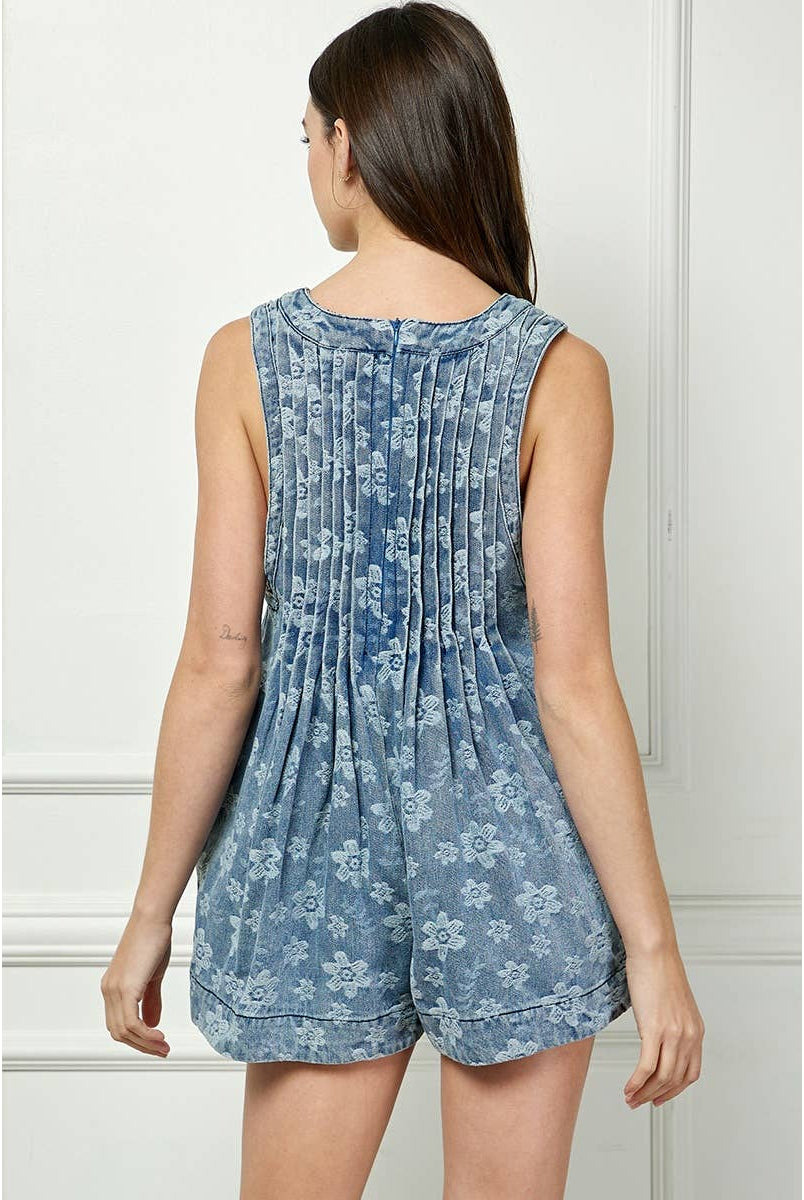 printed denim romper Model wearing the Skylar Tie Front Romper, a sleeveless floral-washed denim romper with pleated front and keyhole tie neckline