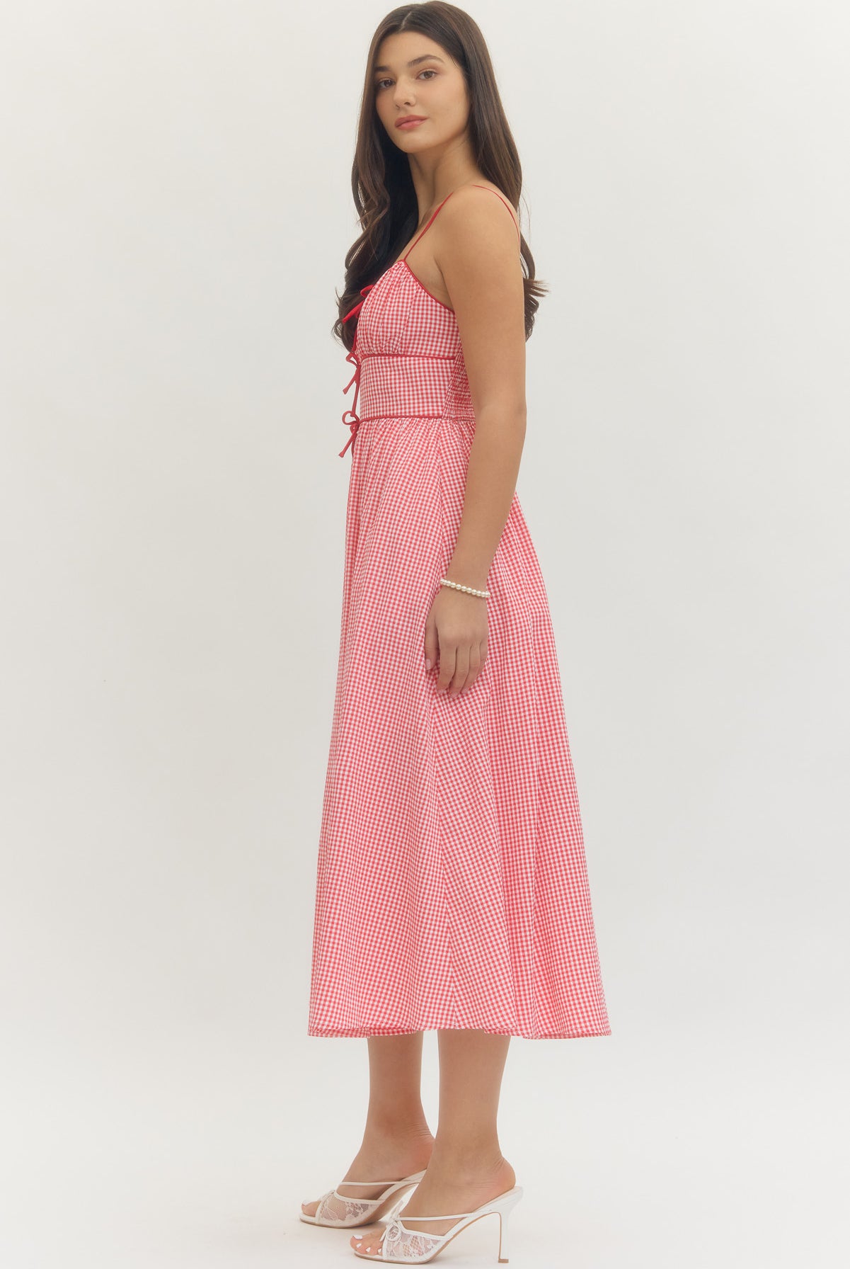 Model wearing a sweetheart gingham maxi dress with adjustable straps, bow details, smocked back, and side pockets in a romantic gingham print, perfect for Valentine’s Day and spring occasions.