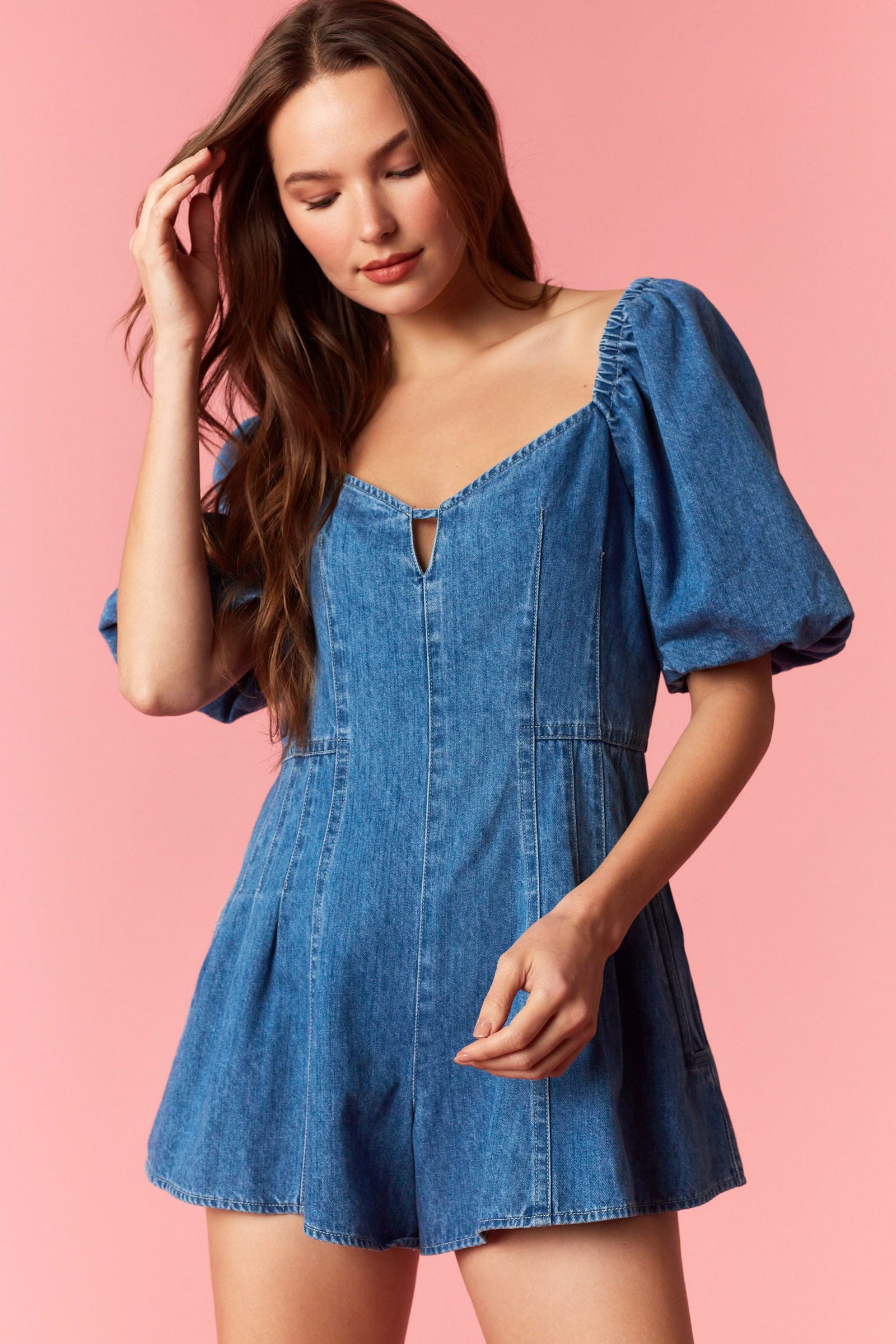 Woman wearing a game day denim romper with bubble sleeves and pleated detail with tie back